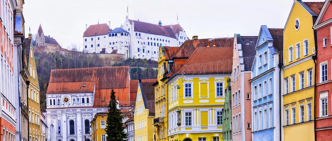 Farbige Giebelhäuser der Landshuter Altstadt, darüber auf dem Hang die weiße Burg Trausnitz