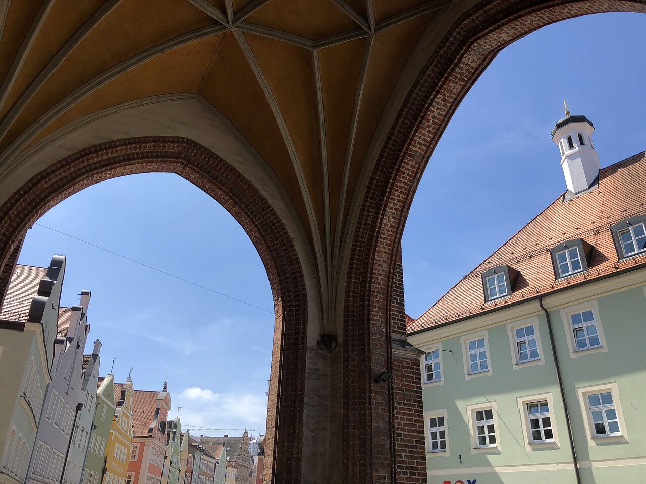 Gotisches Backsteingewölbe mit Rippen in einer Durchfahrt, dahinter farbige Bürgerhäuser der Landshuter Altstadt