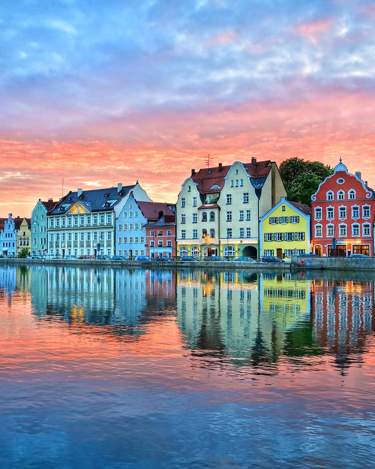 Bunte Häuser am Isarufer in Landshut spiegeln sich im Wasser, darüber ein rot gefärbter Abendhimmel