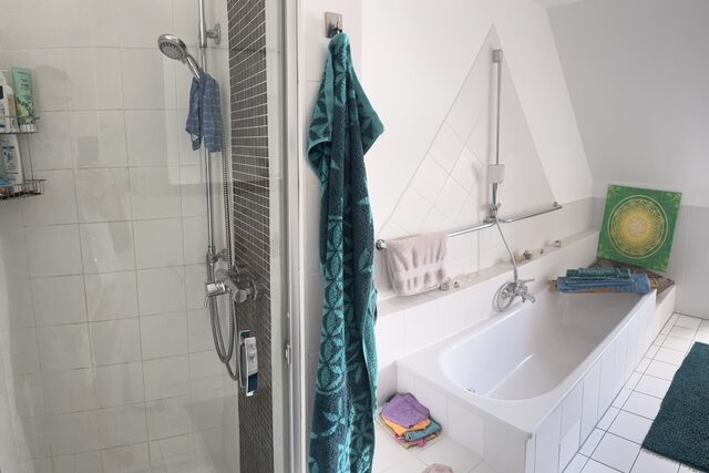Großes Bad mit verglaster Dusche, Badewanne, Handtüchern und hellen Fliesen