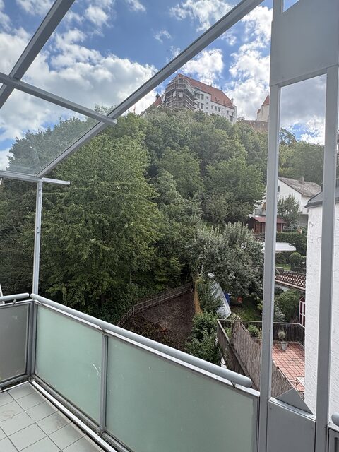 Blick vom überdachten Balkon über bewaldeten Hang hinauf zur Burg Trausnitz in Landshut