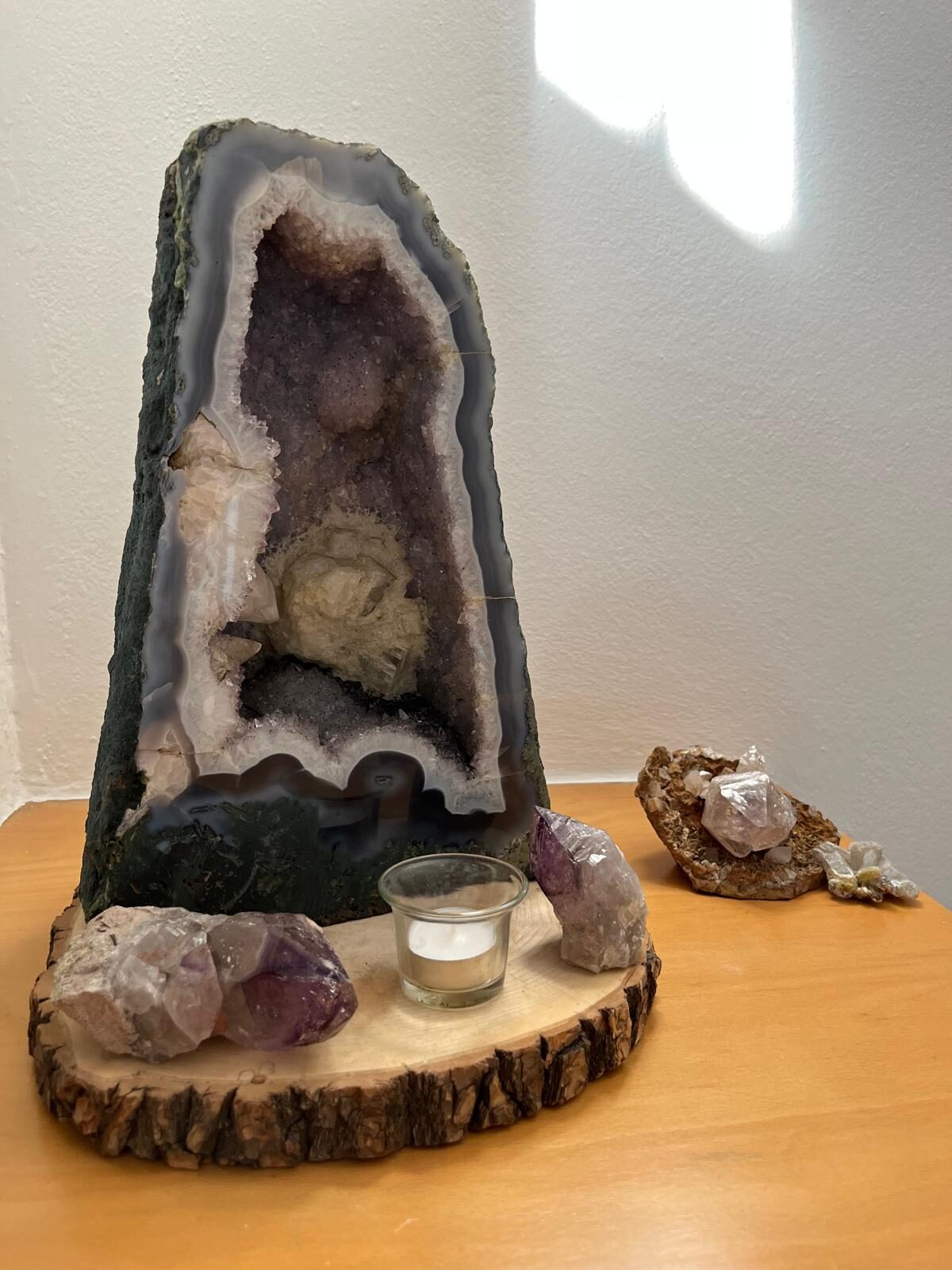 Große Amethyst-Geode mit Kerze und Kristallen auf einer hellen Ablage