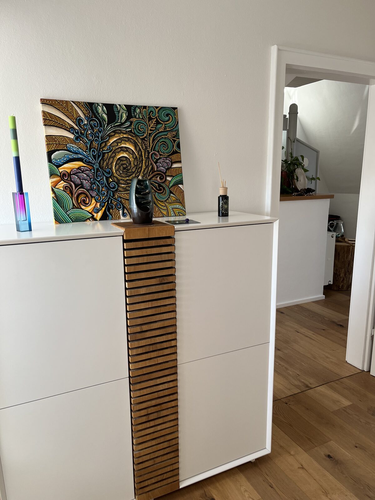 Weißes Sideboard mit Holzelement und einem farbigen Gemälde an der Wand darüber
